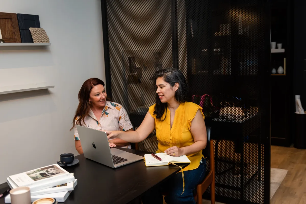 Jane explaining something on a laptop beside another person, with an open notebook on the table.